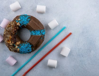 top view chocolate donut with marshmallows and blue with red straws on a gray background